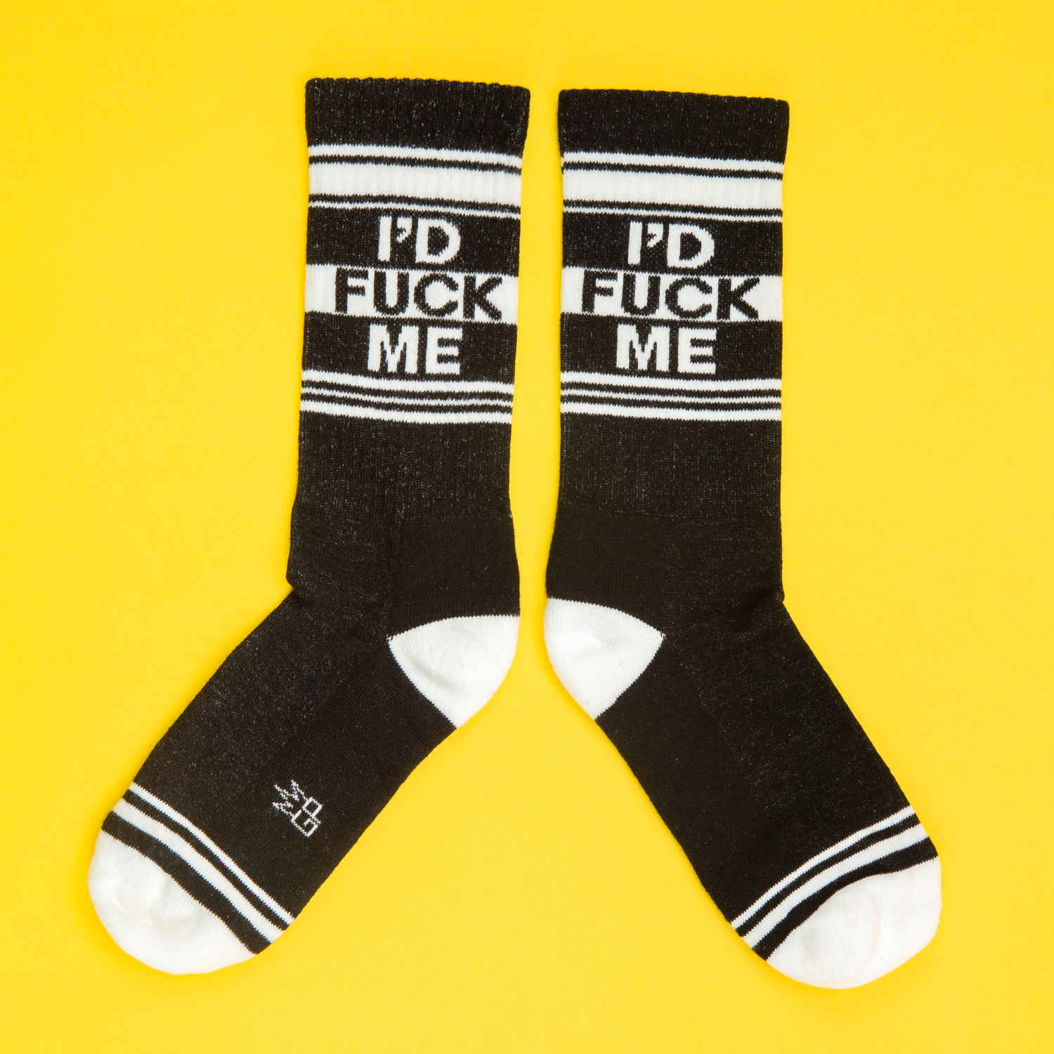 A pair of black and white crew socks that read "I'd fuck me" with the Gumball Poodle logo on the arch.