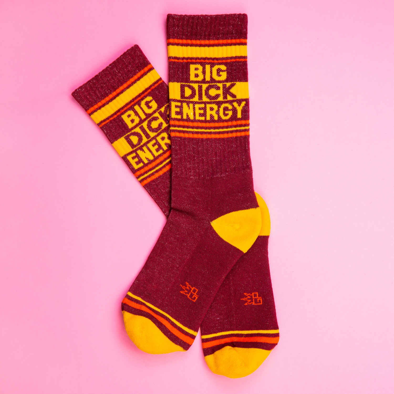 A pair of burgundy and yellow crew socks against a pink background that read "Big Dick Energy" with the Gumball Poodle logo along the arch.